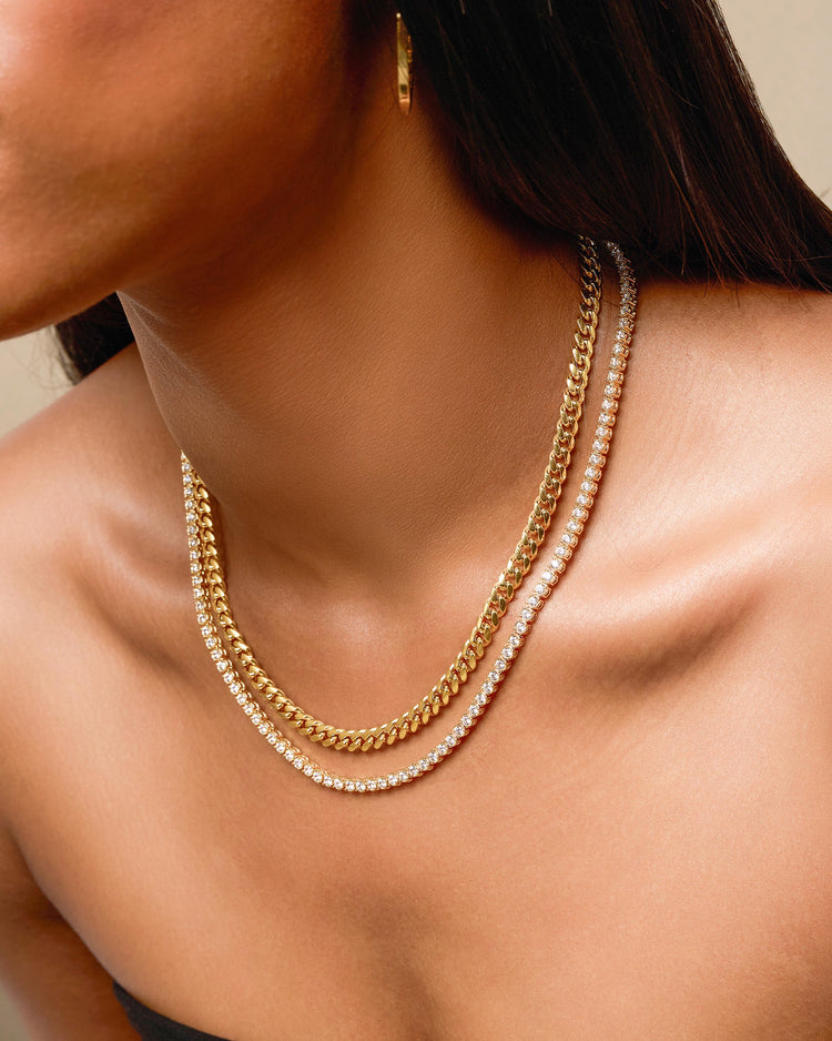 Close-up of a person wearing a gold chain necklace with a neutral background
