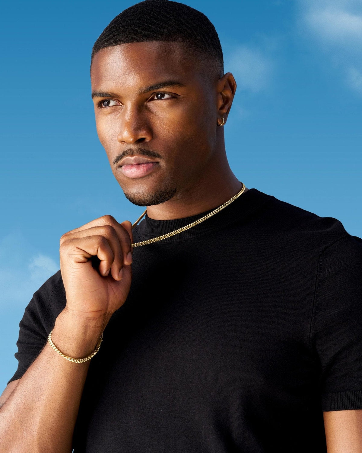 Man wears gold Cuban chain and matching bracelet against a blue sky.
