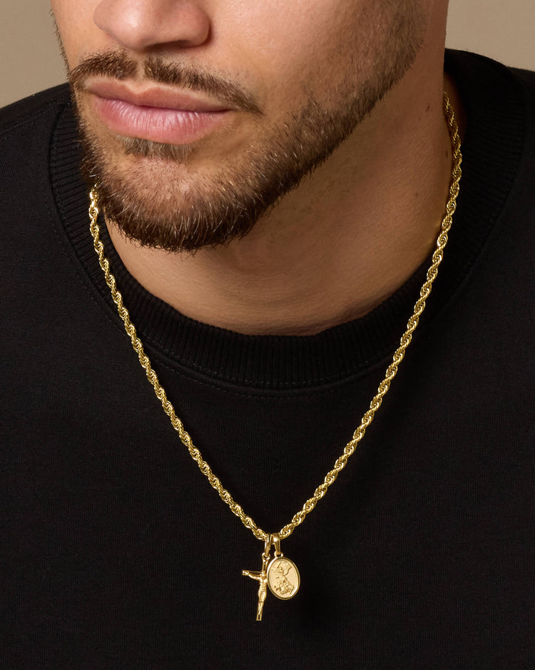 A close-up of a man wearing a gold Rope chain necklace with a crucifix and St. Michael medallion pendant, styled with a black crewneck shirt.