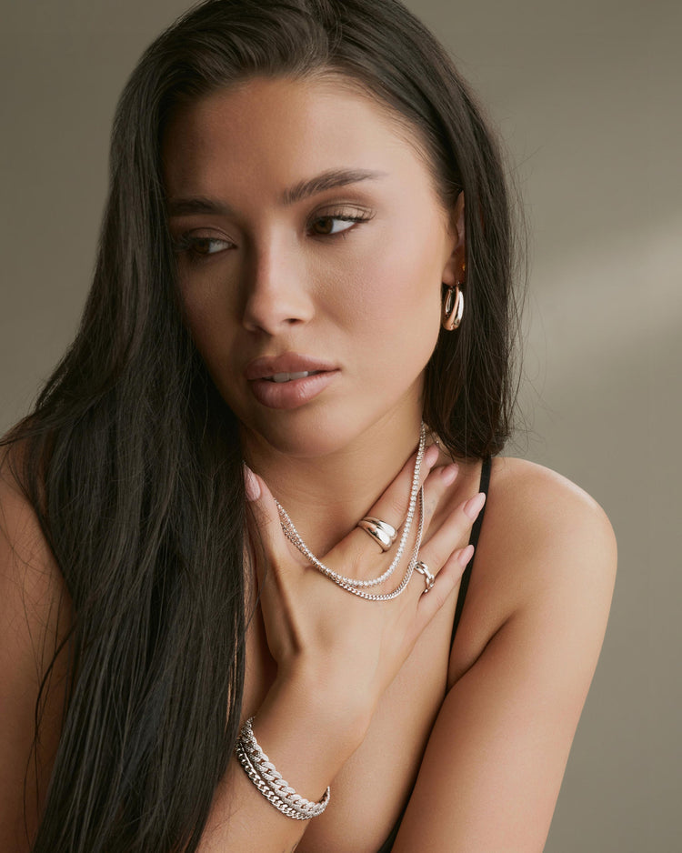 Woman wearing multiple pieces of jewelry including a necklace, ring, and bracelet against a neutral background.