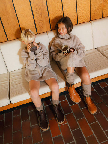 Two children on a bench sipping hot drinks in brown barefoot boots
