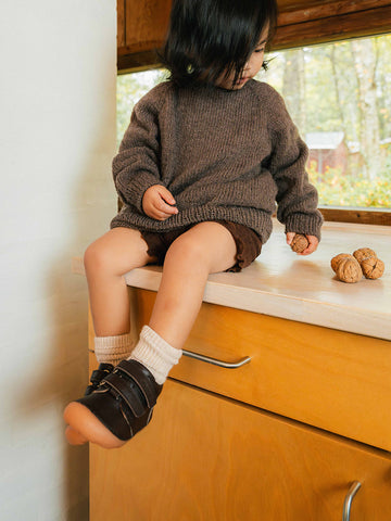 A toddler on a kitchen counter in brown first step shoes