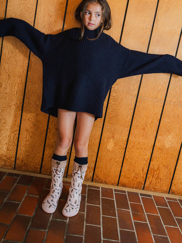 A girl in a navy jumper with arms spread wearing patterned rubber boots