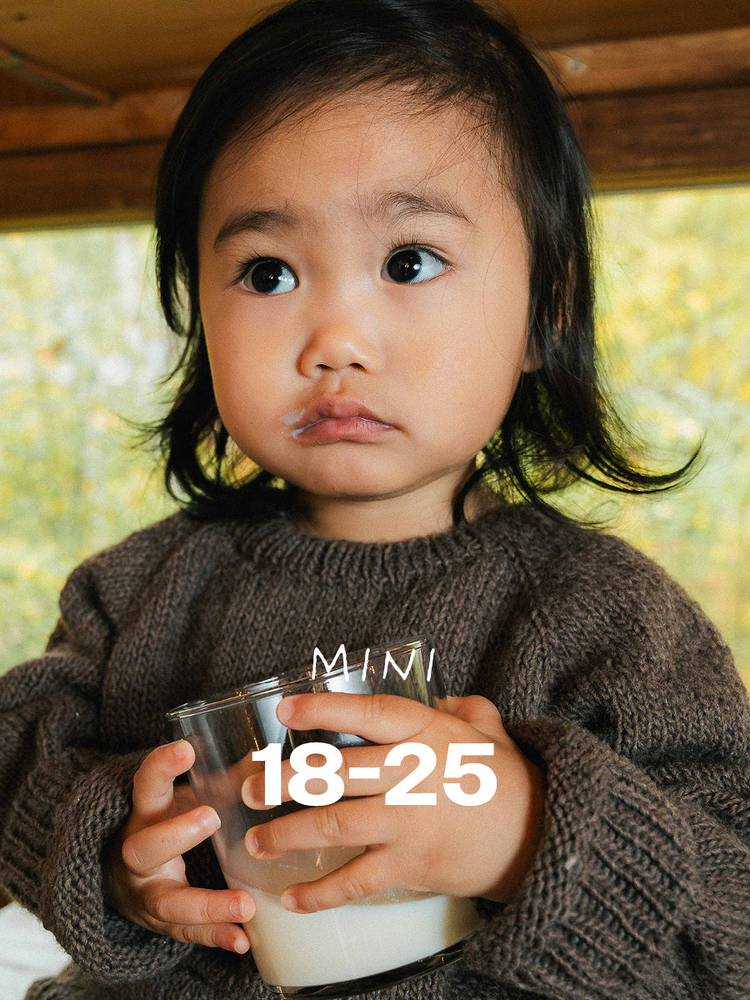 A toddler in a brown knitted jumper holding a glass of milk