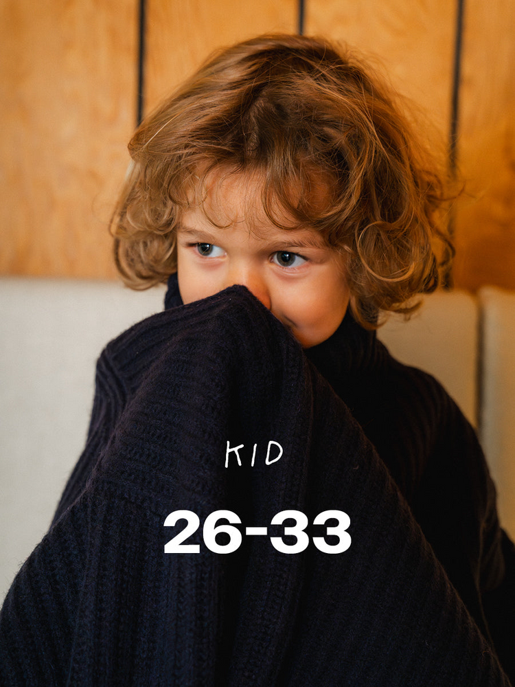 A curly-haired child hiding behind a navy knitted jumper