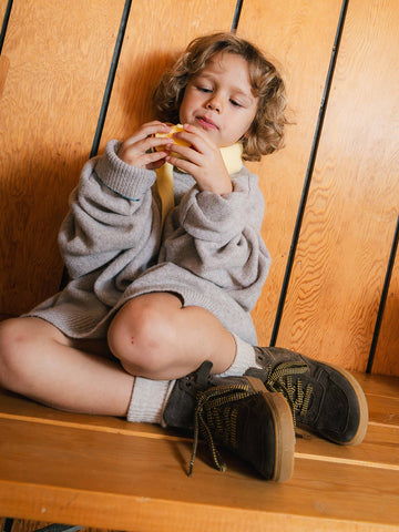 A boy sitting cross-legged on a bench in dark lace-up sneakers